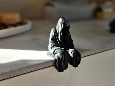 Grim reaper figurine perched on a shelf edge